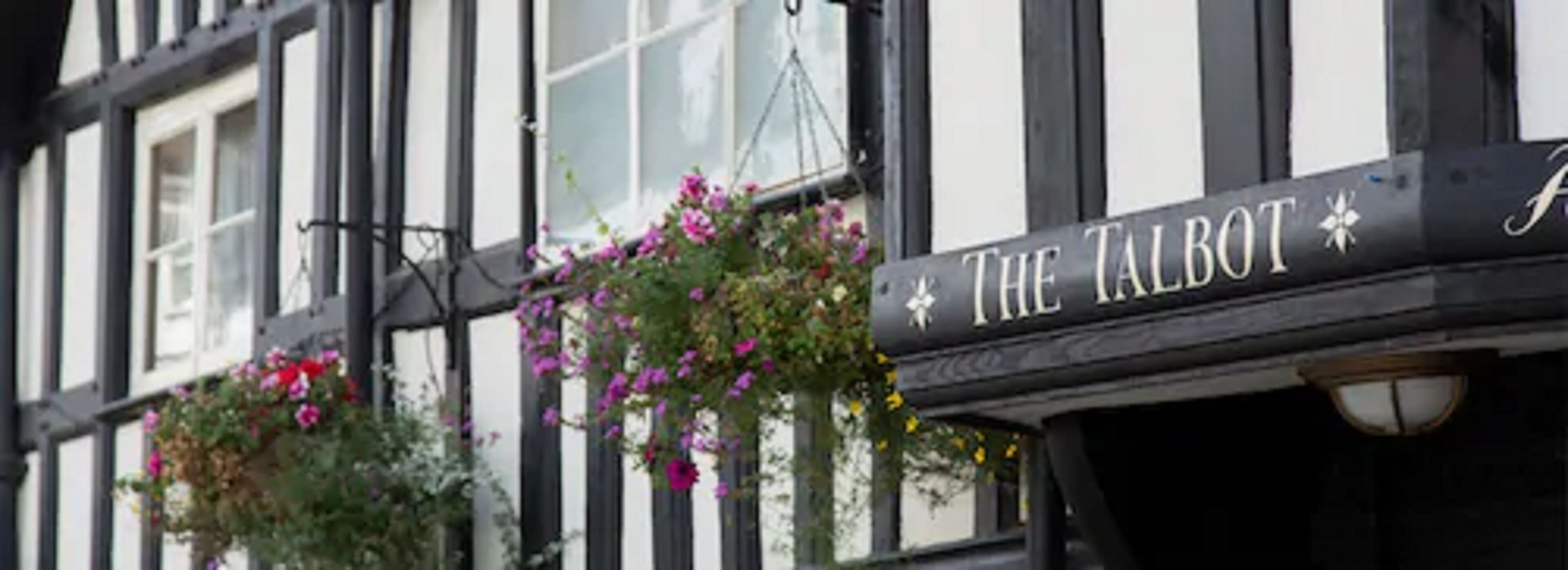 A building with black and white timber framing, a sign reading "The Talbot," and hanging flower baskets.
