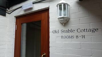 A white brick wall with a wooden door and a sign reading "Old Stable Cottage ROOMS 8-14".
