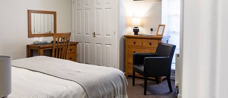 A bedroom with a bed, a wooden desk, a chair, a dresser, a mirror, and a television.