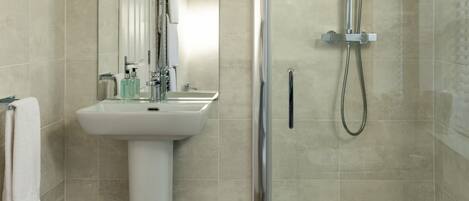 A modern bathroom with a pedestal sink, a glass-enclosed shower, and a wooden floor.
