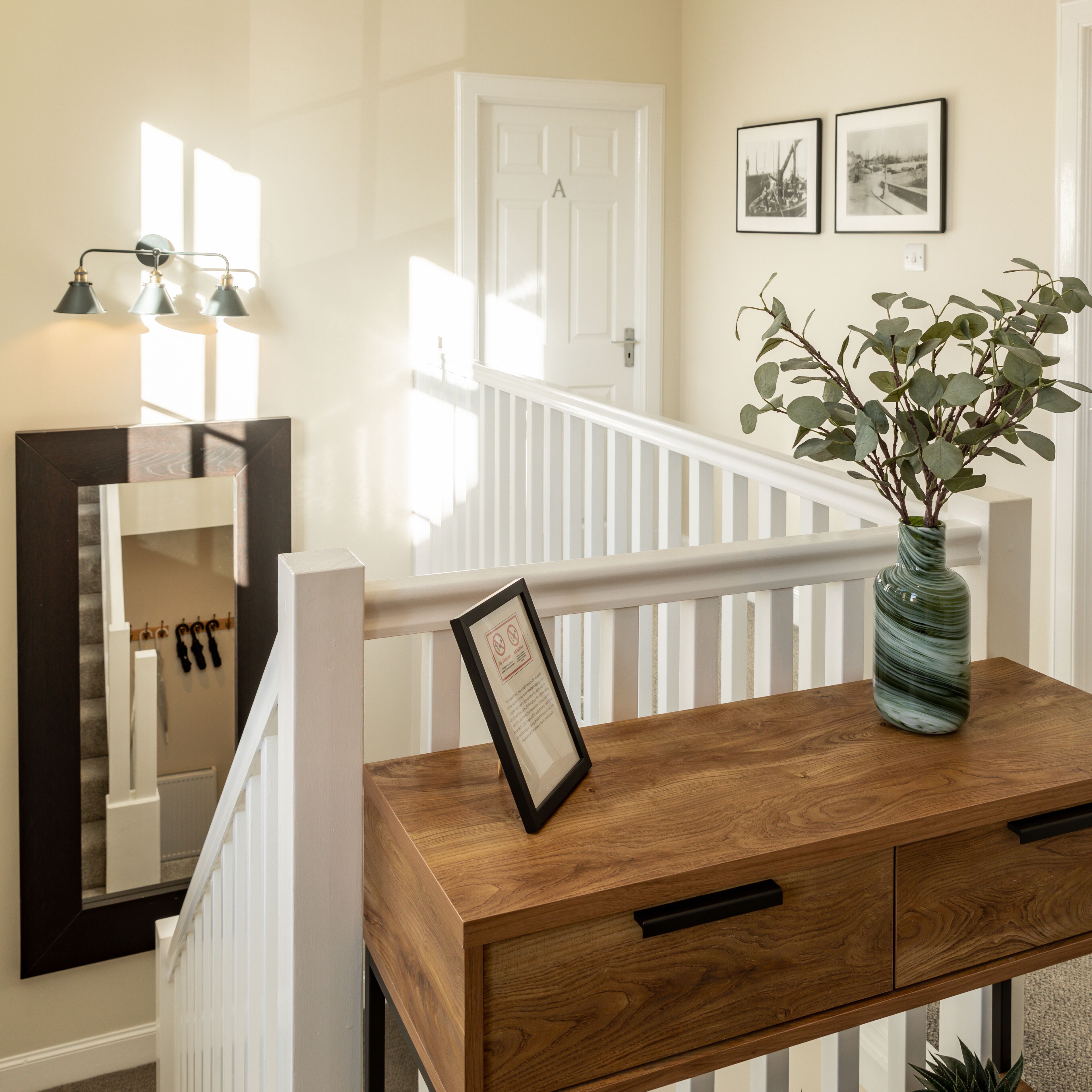 A wooden console table with a framed certificate, a vase with green foliage, and a mirror on the wall.