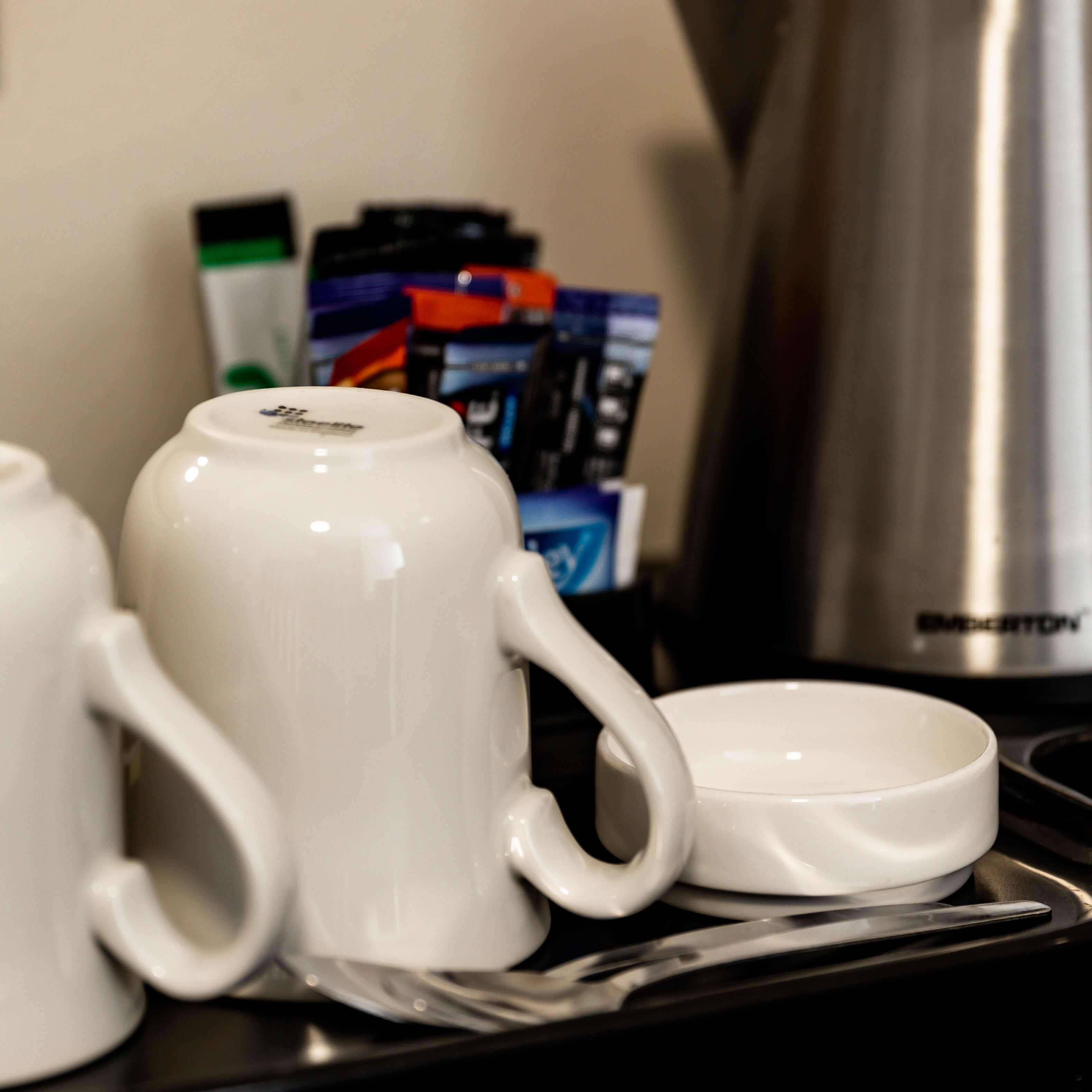 Une machine à café, une tasse et une soucoupe sur une table, avec une boîte de capsules de café en arrière-plan.