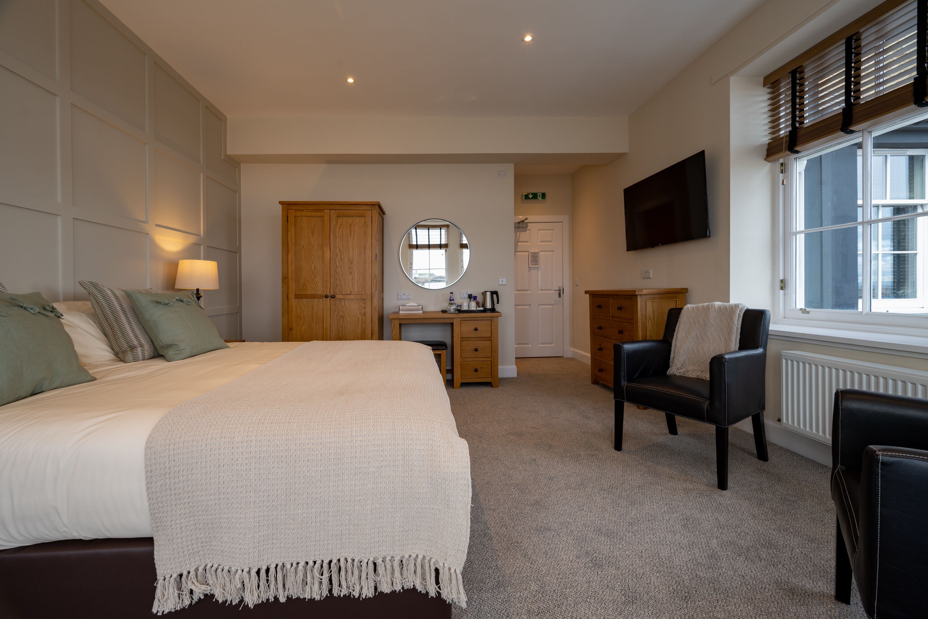A bedroom with a large bed, a desk, a chair, a TV, and a window.