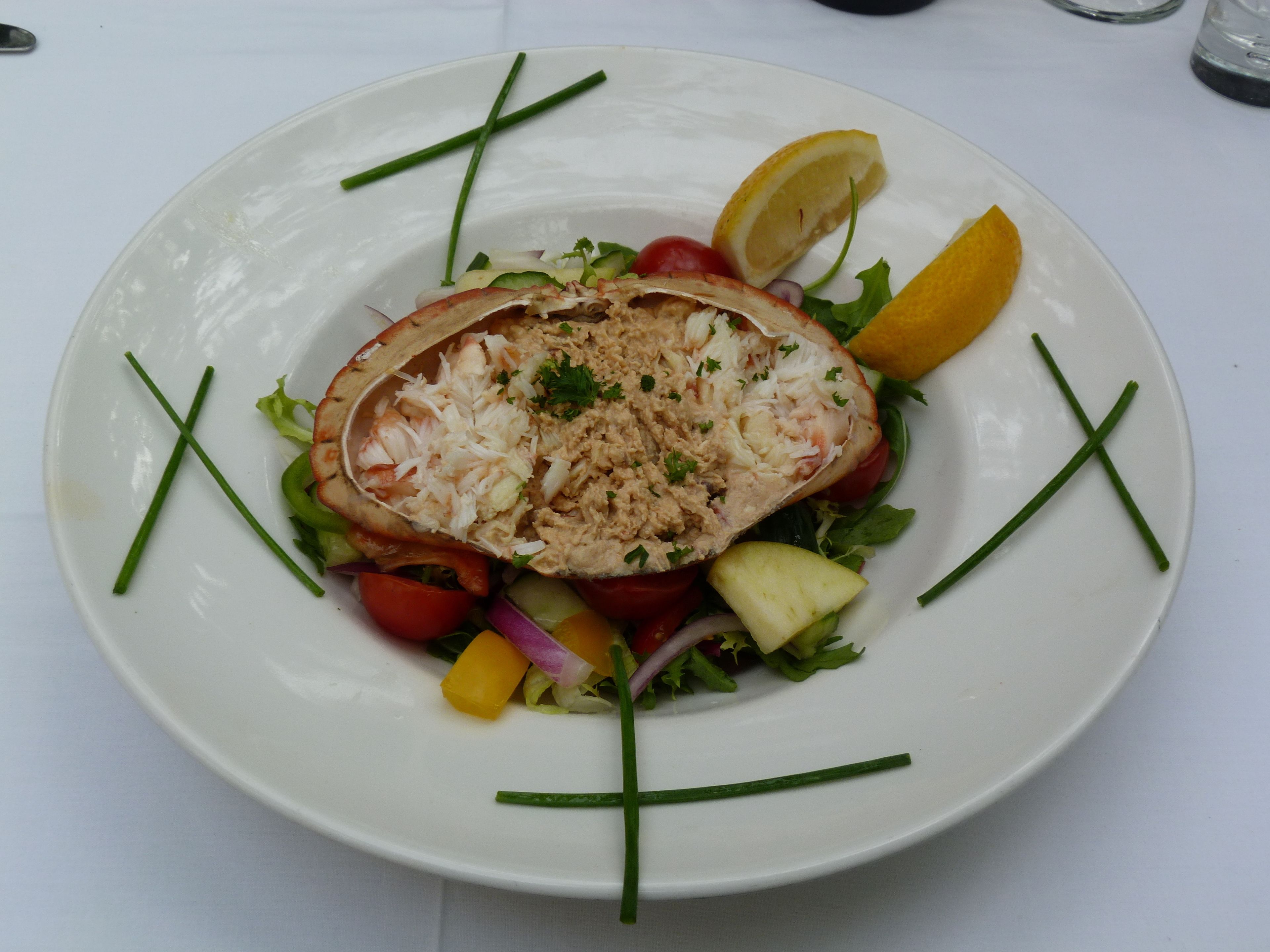 A plate of food with a salad and a stuffed item, garnished with lemon and chives.