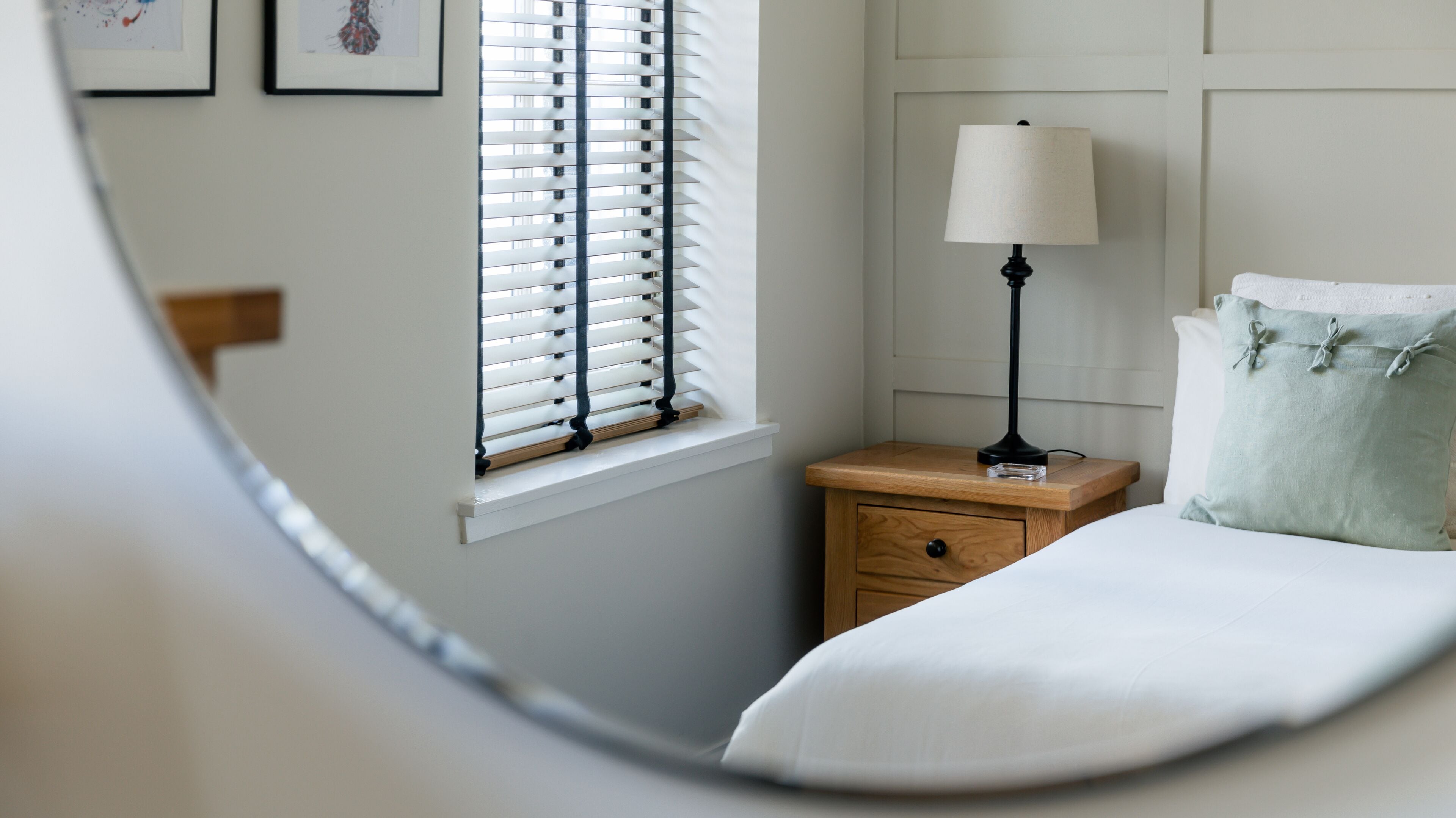 A bedroom with a bed, a nightstand, a lamp, and a window with blinds.