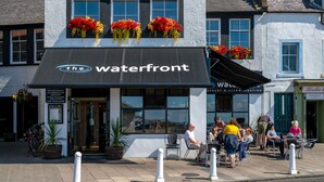 Un restaurante frente al agua con terraza, macetas y jardineras en las ventanas.