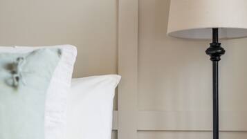 A neatly made bed with white and light blue pillows, a black lamp on a wooden nightstand, and a clear glass object on the nightstand.