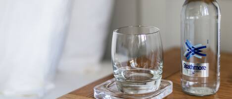 A bottle of Strathmore still spring water and an empty glass on a wooden coaster.