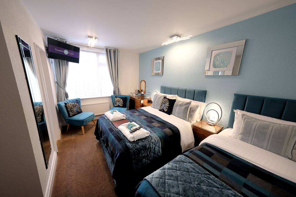 A hotel room with two beds, a TV, a desk with a lamp, and a window with curtains.