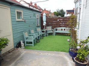 Un patio trasero con césped verde, valla de madera y mobiliario exterior, incluyendo sillas y una mesa.