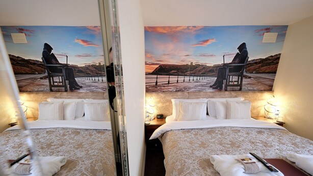 A hotel room with two beds, a large painting of a sunset scene, and a mirror reflecting the room. - Toulson Court (Scarborough)