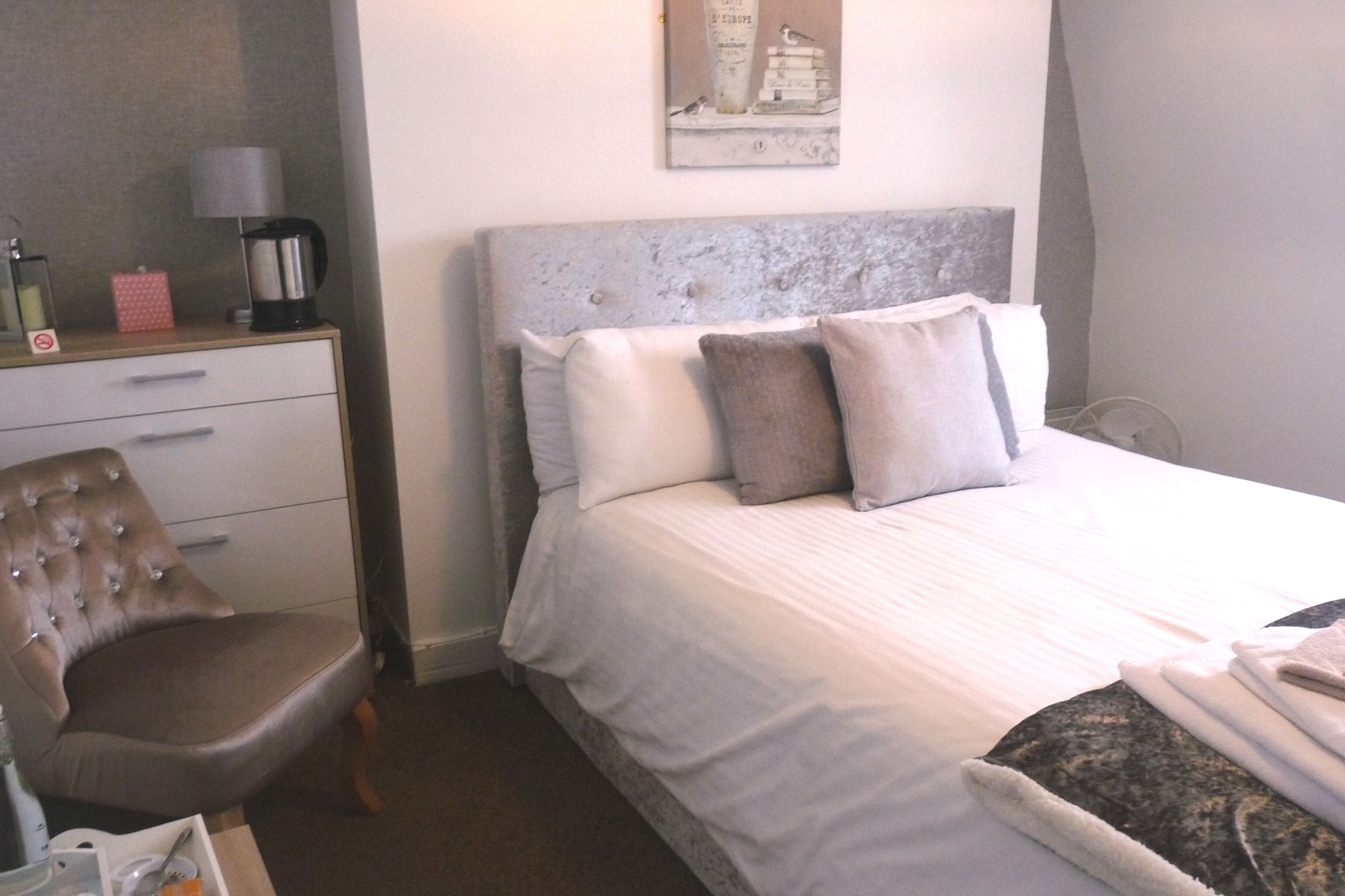 Une chambre d’hôtel avec un lit, une chaise, un bureau avec une lampe, une machine à café et un tableau au mur.