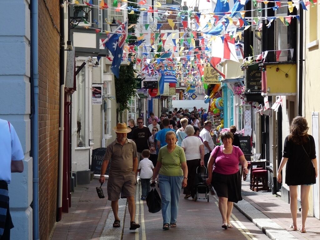 Une rue étroite bordée de boutiques et de cafés, décorée de drapeaux et de banderoles aux couleurs vives.