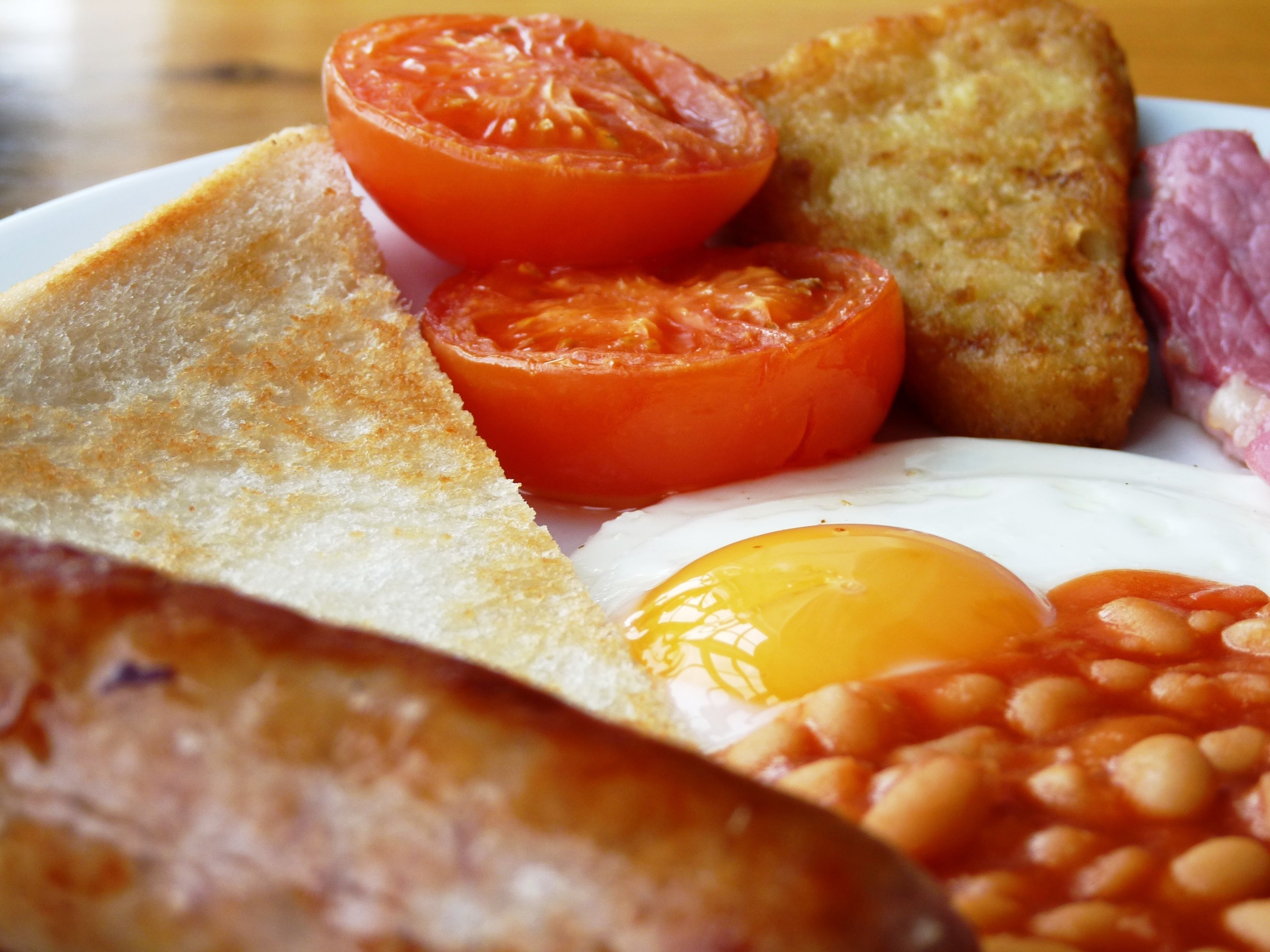 A plate of breakfast food including toast, eggs, tomatoes, beans, and sausage.