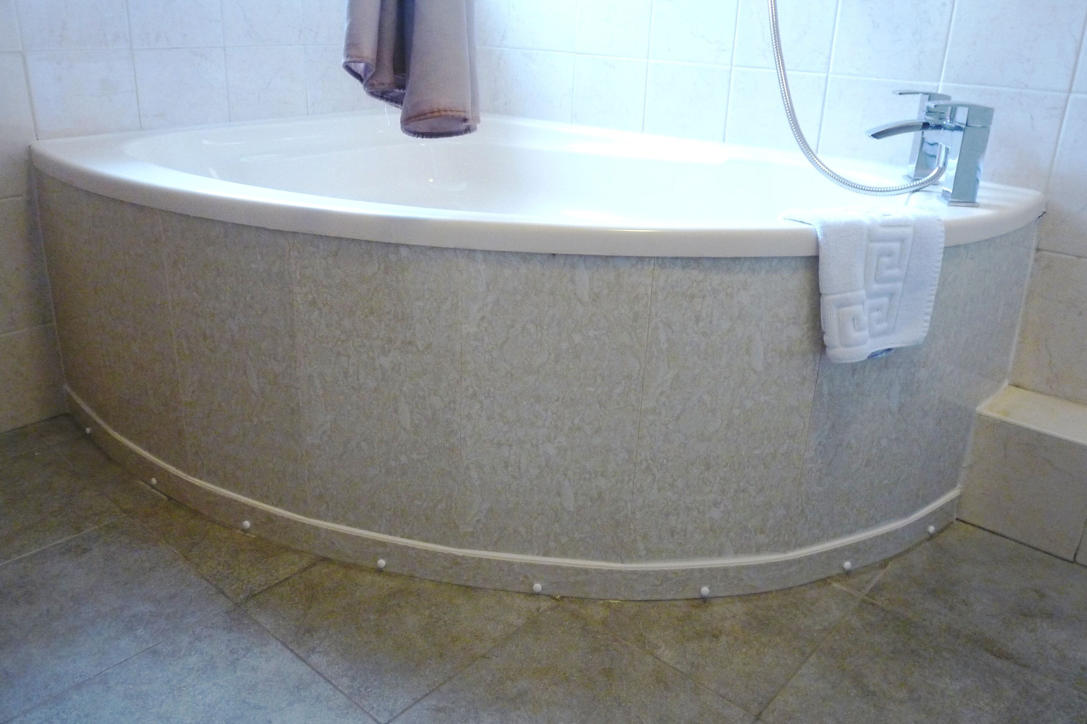 A large, freestanding bathtub with a showerhead, set against a tiled wall.
