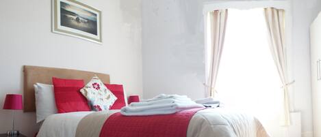 A neatly made bed with red and white bedding, a bedside lamp, and a framed picture on the wall.
