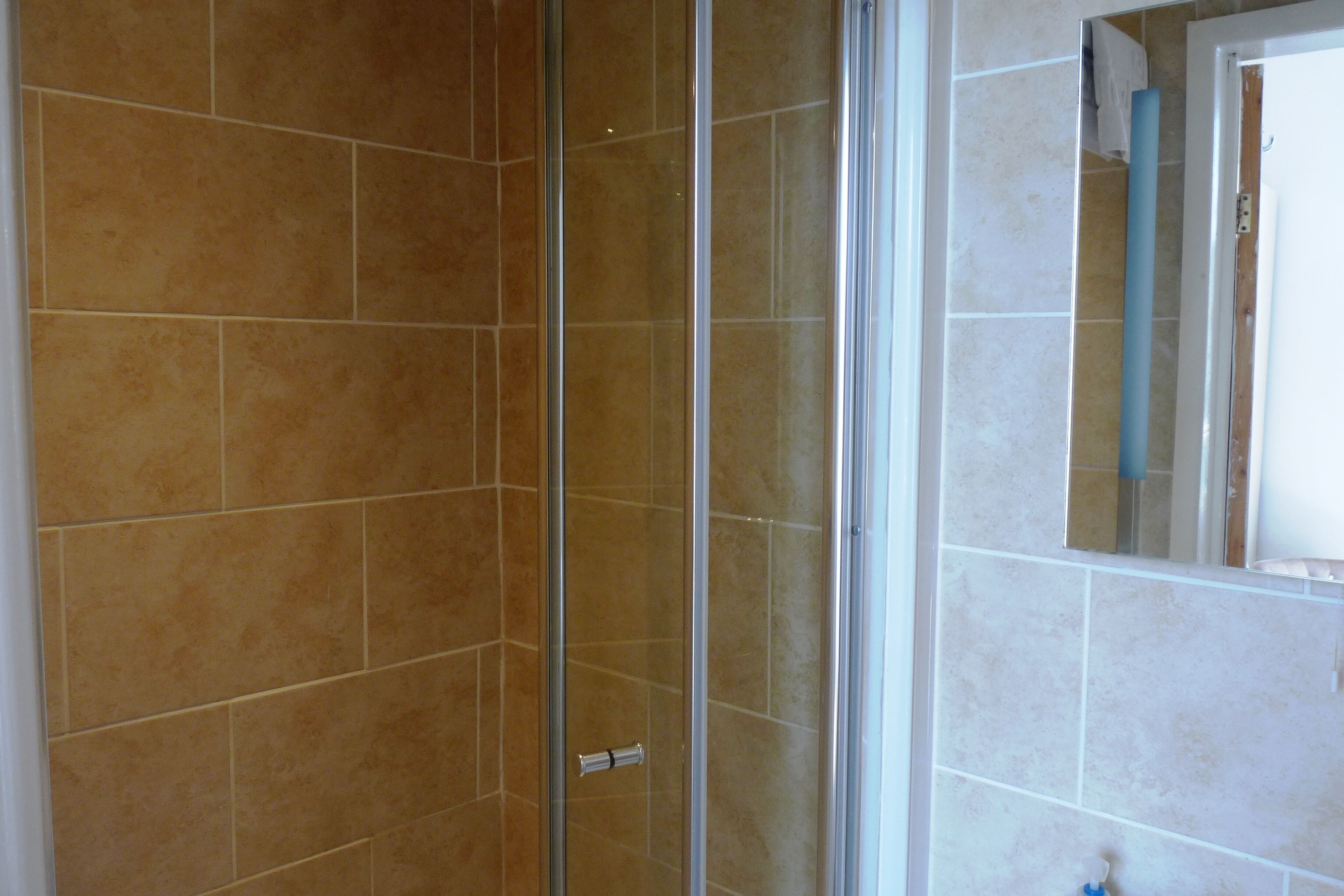 A bathroom with beige tiles, a glass shower enclosure, and a mirror.