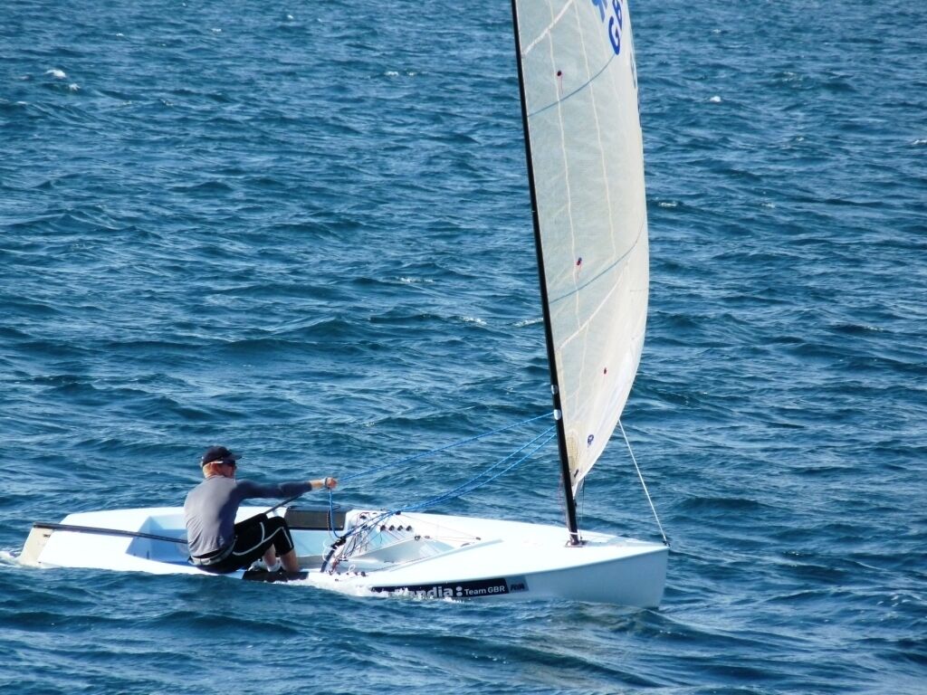 Un velero con una persona manejando, sobre una masa de agua.