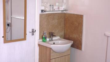 Une salle de bain avec un lavabo blanc, un miroir et une étagère contenant des articles de toilette.