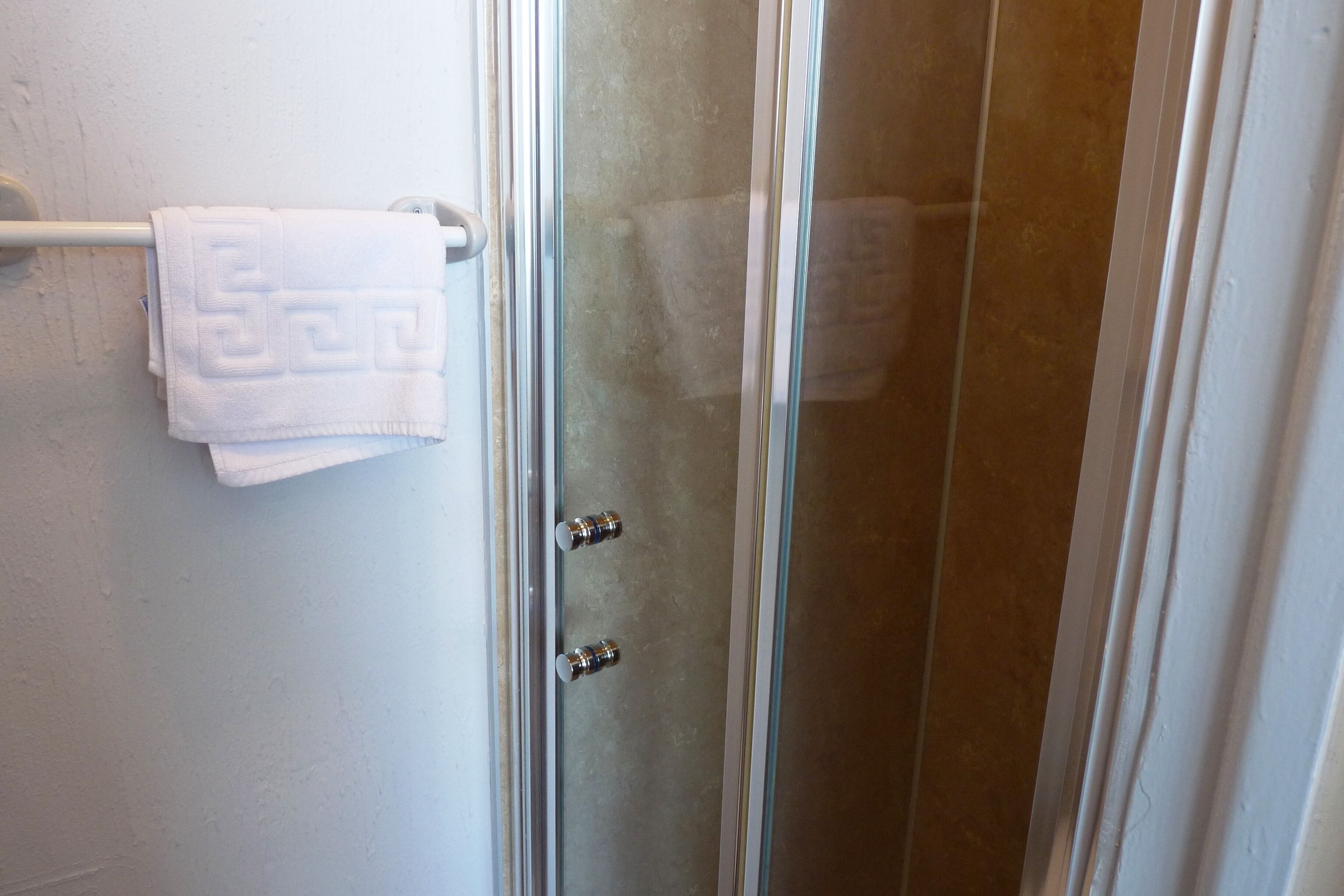 A bathroom with a glass shower door, a white towel hanging on a towel rack, and a white wall.