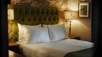 A neatly made bed with white linens and a green upholstered headboard. There are two bedside lamps and a framed picture on the wall.