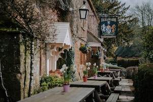 Un área de estar al aire libre con mesas y sillas de madera, un edificio de ladrillo cubierto de hiedra y un letrero que dice "Falkland Arms, Vadworth".