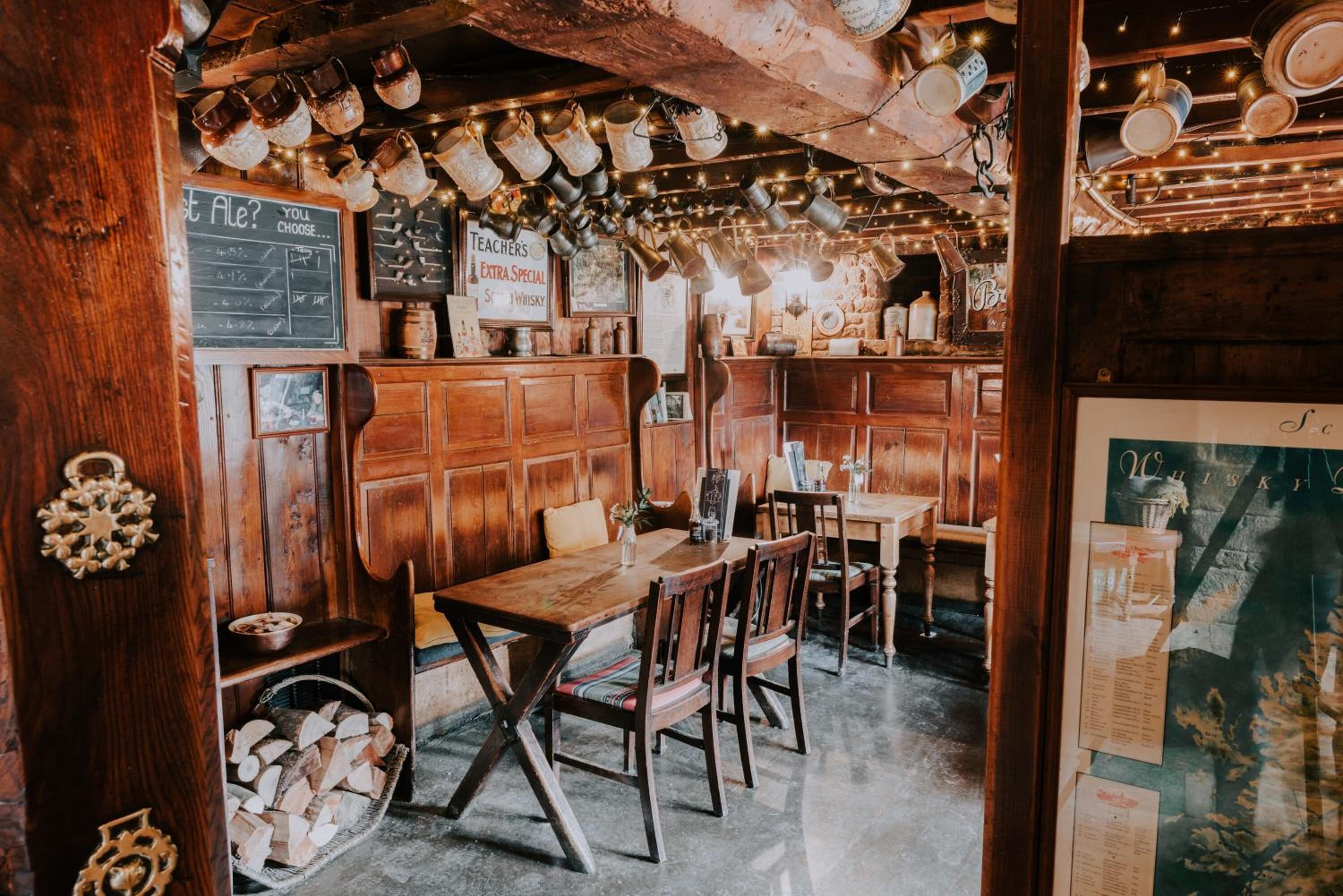 Un intérieur rustique avec des lambris en bois, un tableau noir servant de menu et divers récipients en métal suspendus au plafond.