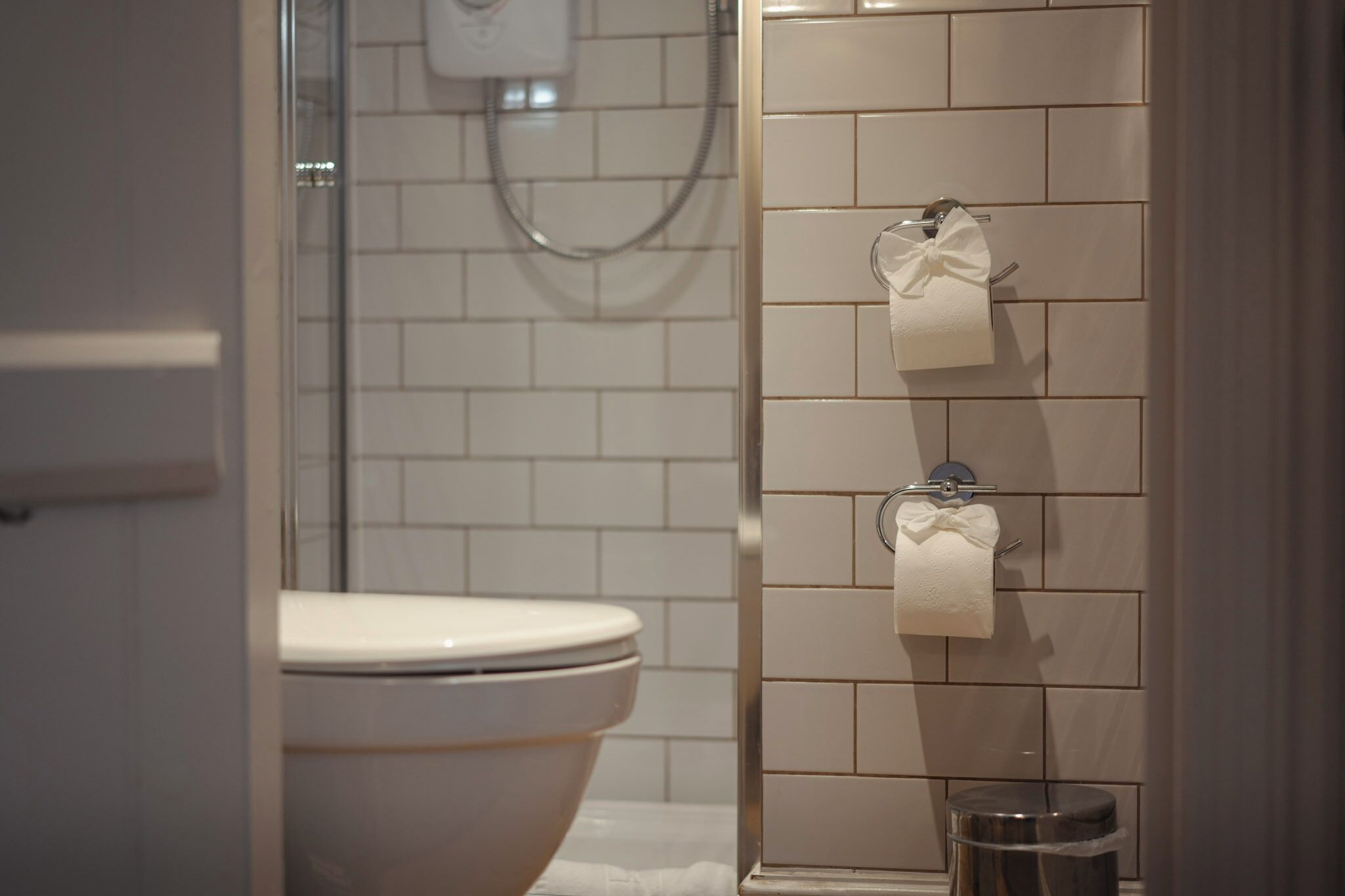 Un baño con inodoro, ducha con puerta de vidrio y dos rollos de papel higiénico en la pared.