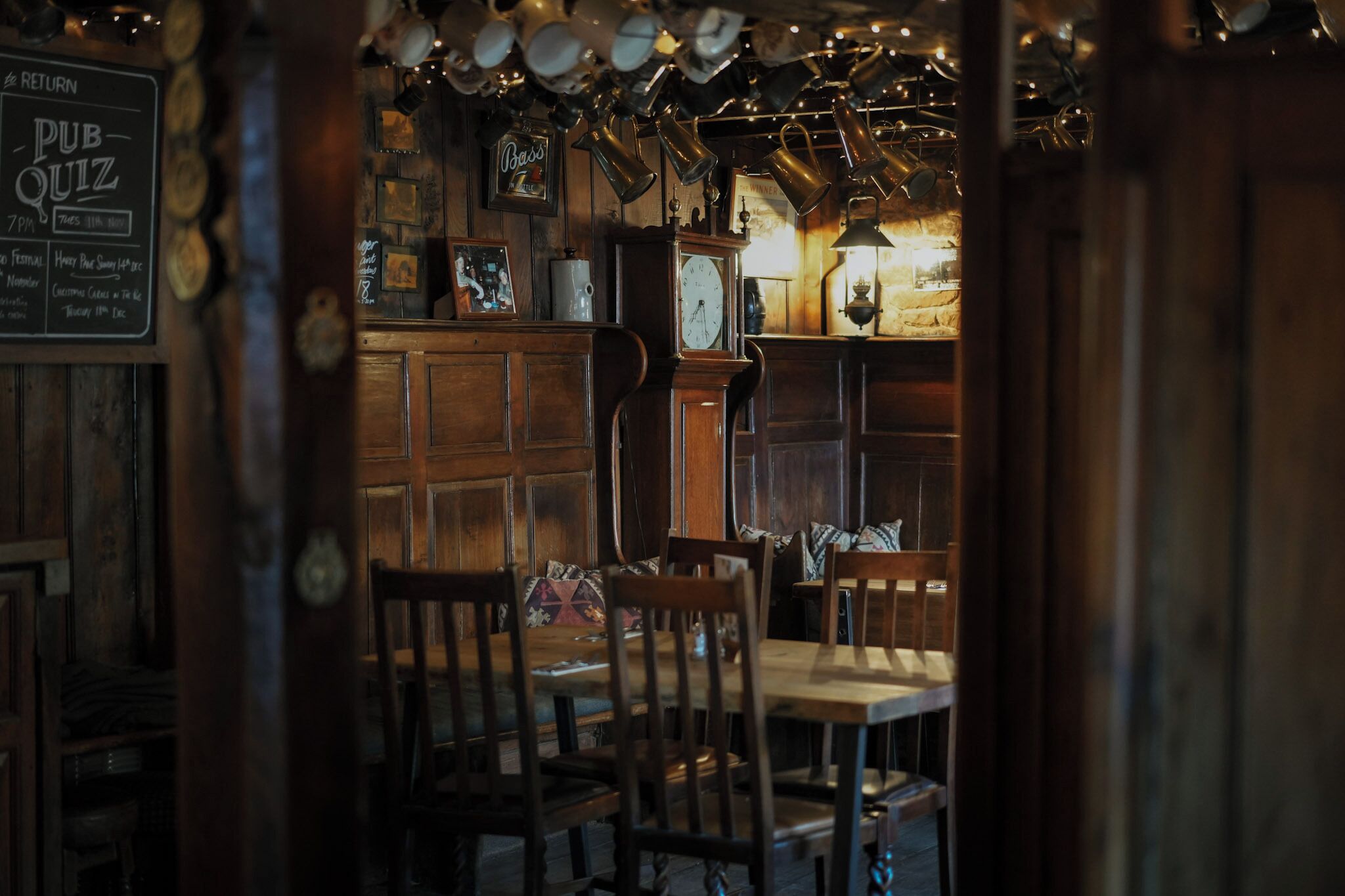 A pub interior with wooden furniture, a clock, and a sign for a pub quiz.