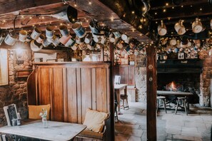 A rustic interior with wooden walls, a stone fireplace, and a table with chairs. - The Falkland Arms (Chipping Norton)