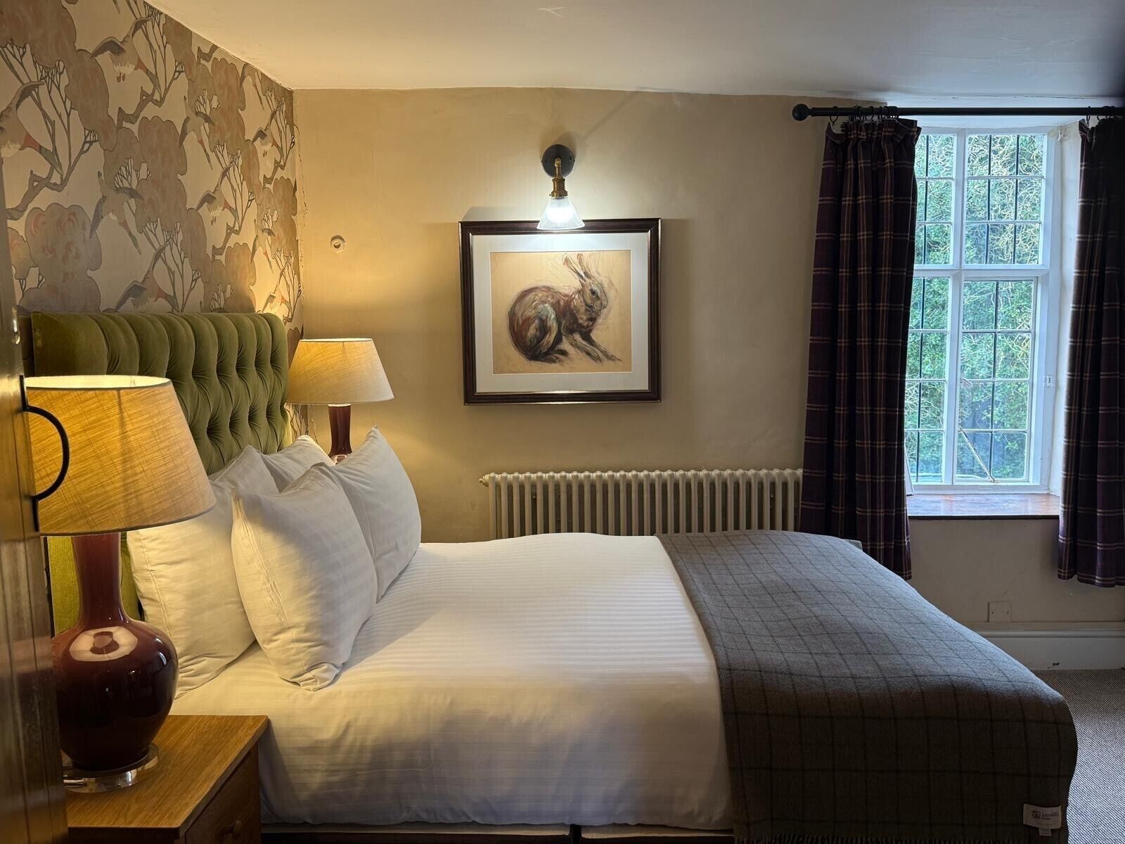 A neatly made bed with white linens, a green upholstered headboard, and a framed artwork above it.