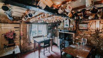 Un pub rústico con paredes de piedra vista, vigas de madera y una variedad de jarras colgando del techo.