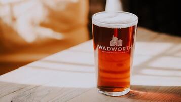 A glass of beer with the label "WADWORTH BREWED IN WILTSHIRE SINCE 1875" on a wooden table.