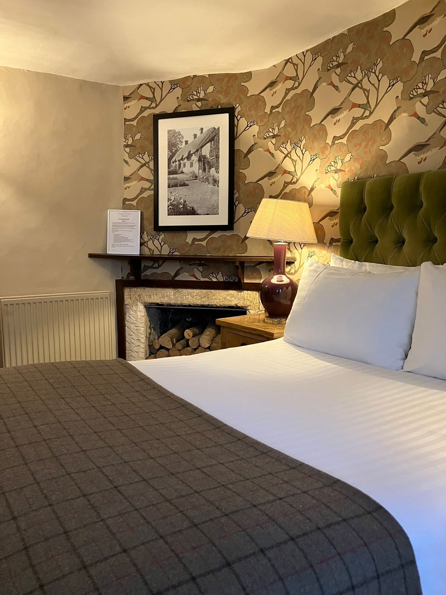 Een hotelkamer met een groot bed, een open haard, een inlijsting foto aan de muur en een lampje op het nachtkastje.