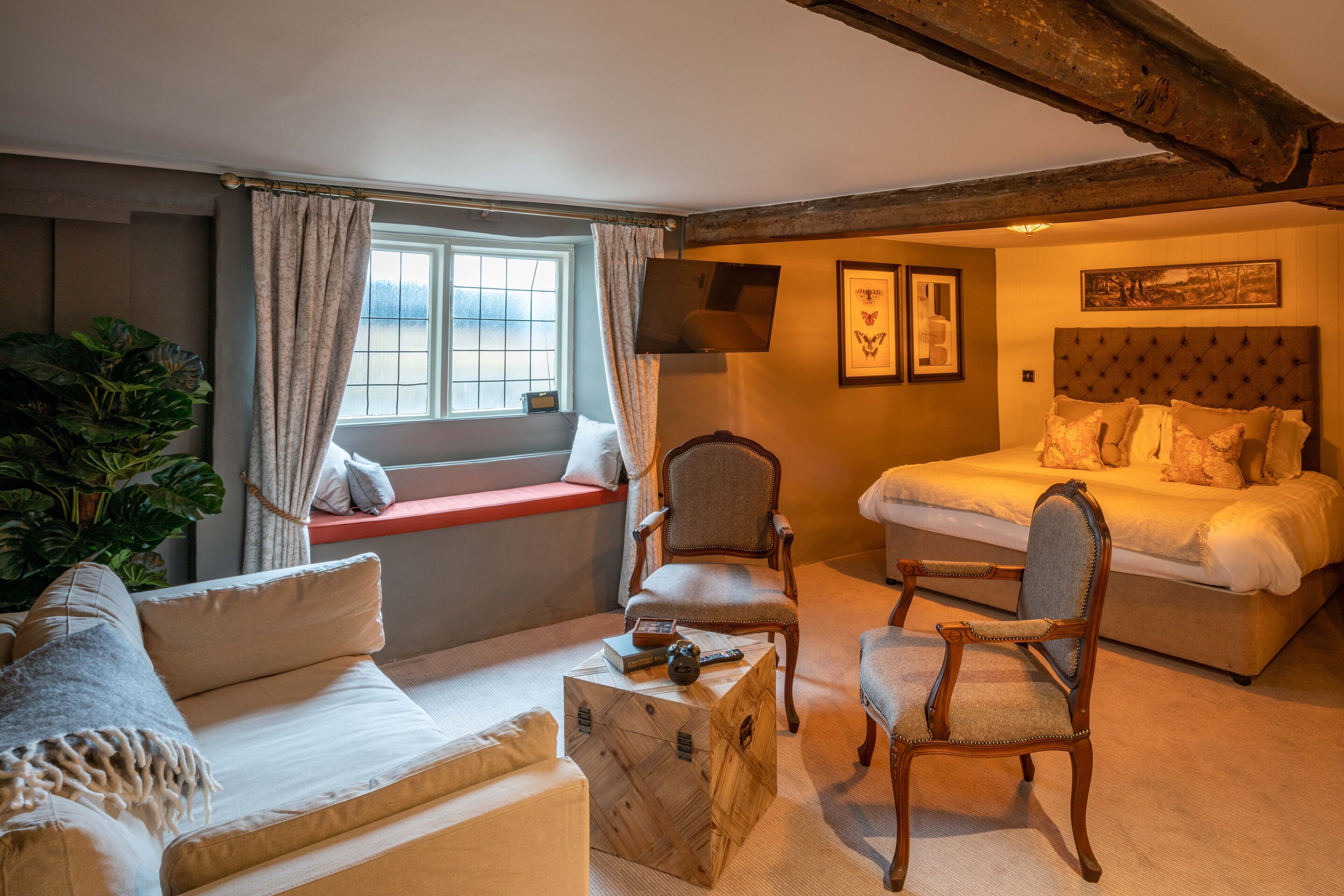 Een gezellige kamer met een bed, twee fauteuils, een bank en een raam met gordijnen.