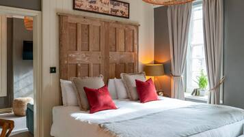 A bedroom with a large bed, two red pillows, a wooden headboard, a wall-mounted TV, and a window with curtains.