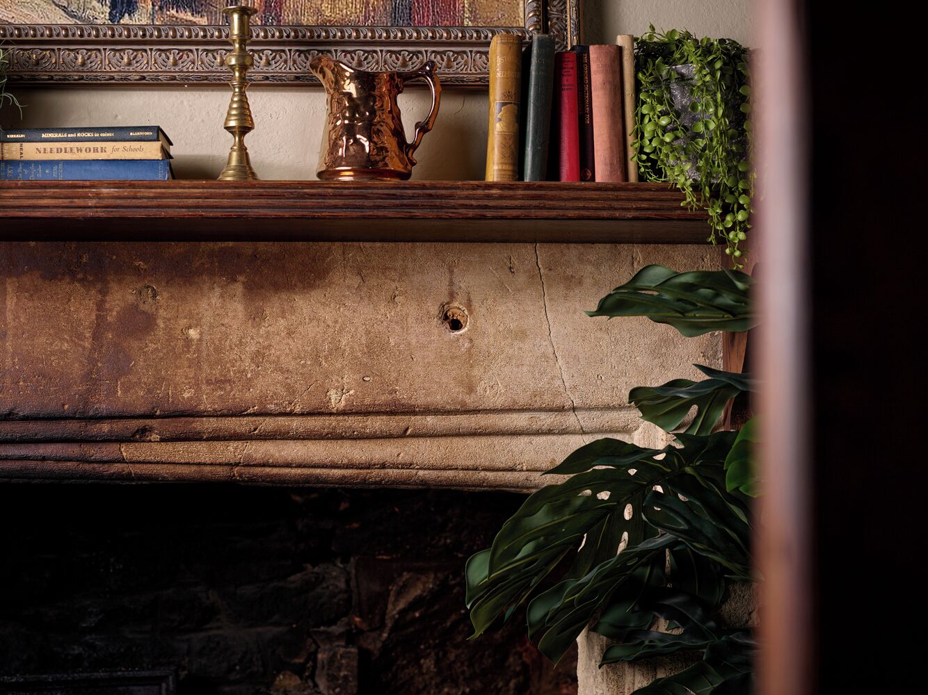 Una repisa de chimenea con libros, una jarra de bronce y una planta.