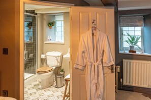 Une salle de bain avec douche, toilettes et peignoir suspendu.