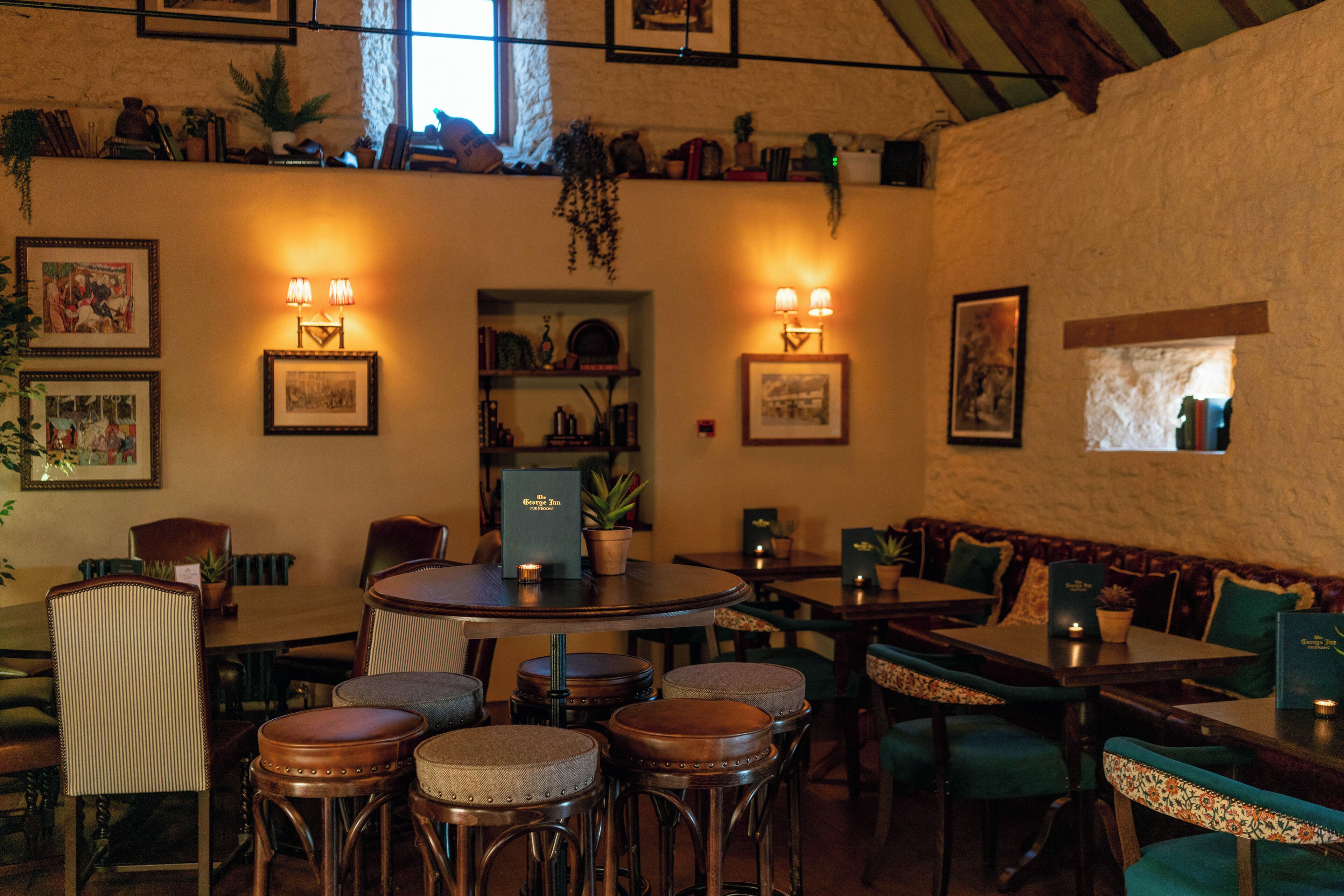 A restaurant interior with round tables, bar stools, and green upholstered chairs.