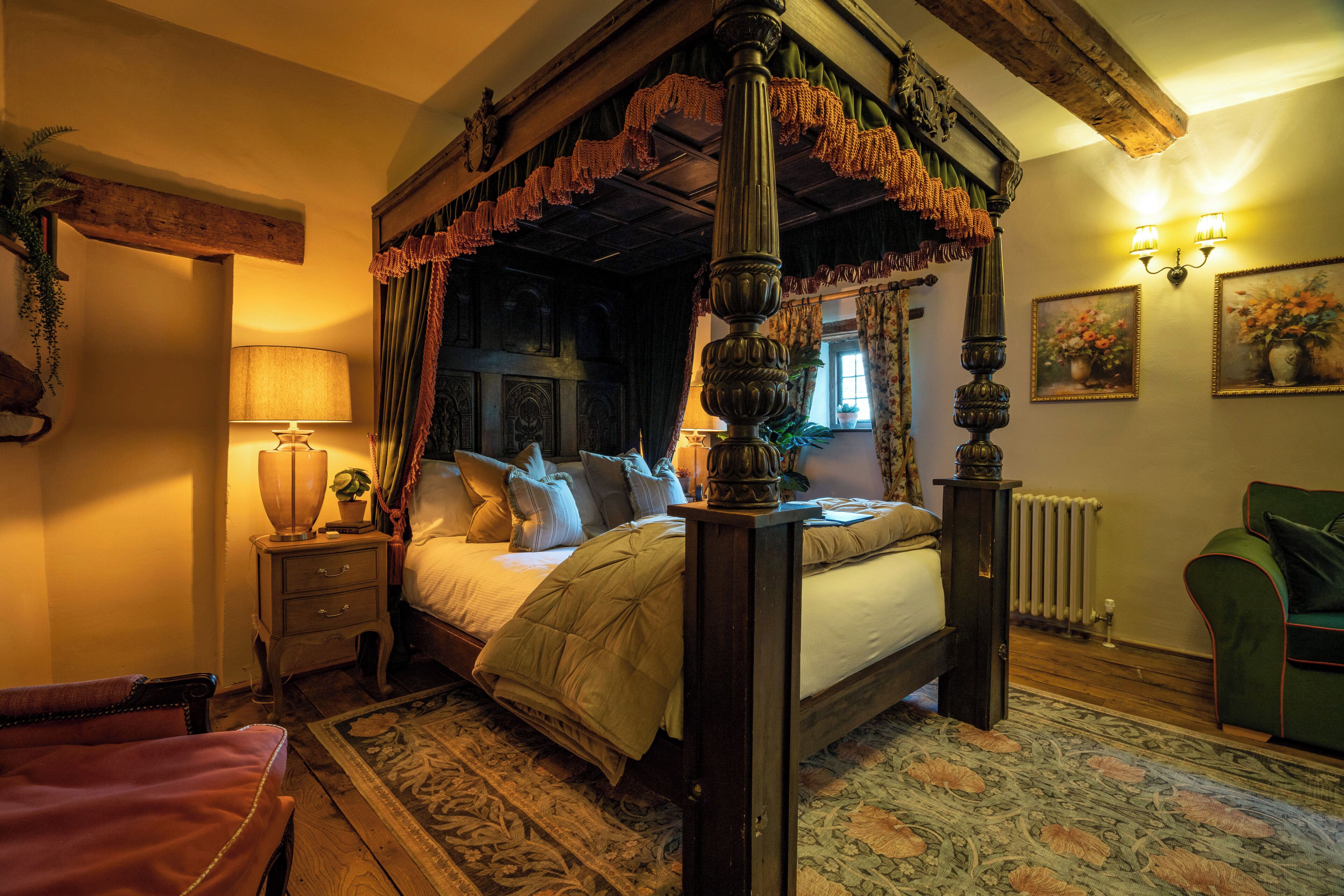 A four-poster bed with a canopy, a nightstand with a lamp, a green armchair, and a radiator.