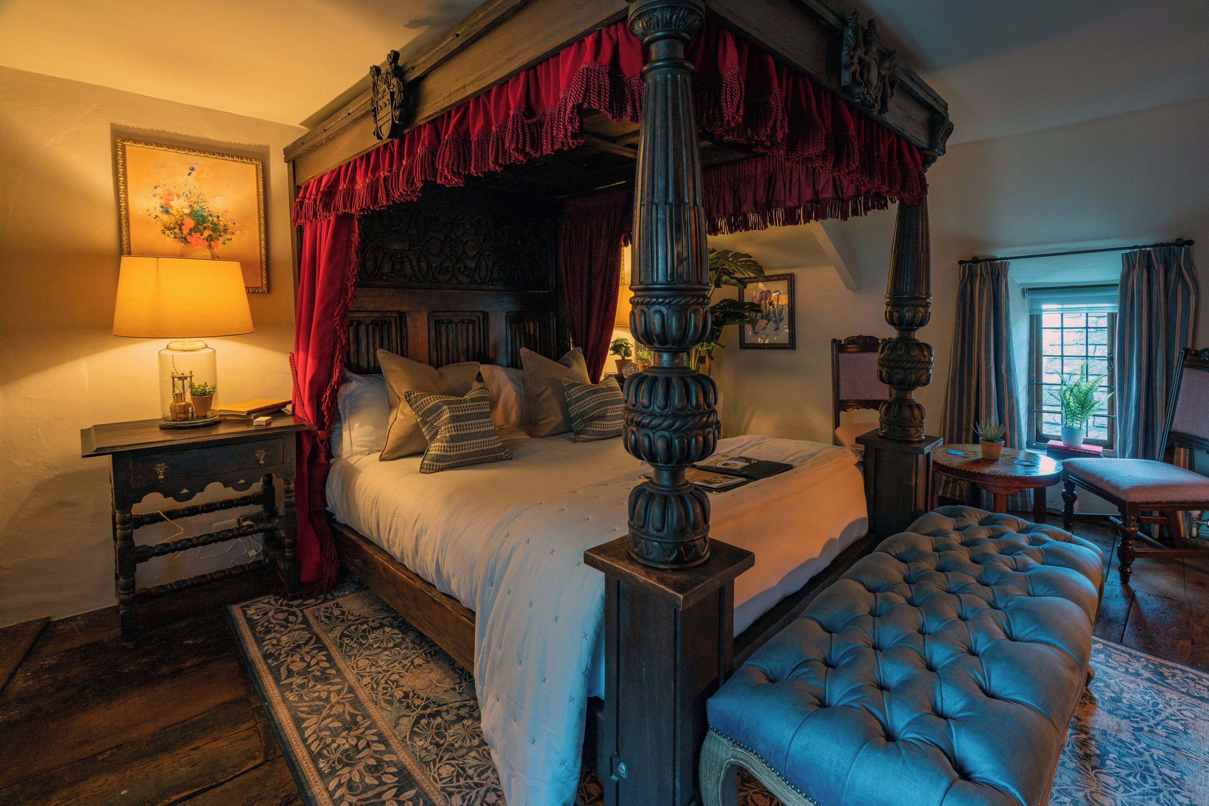 A four-poster bed with a canopy, a bedside table with a lamp, a chair, and a small table with a plant.