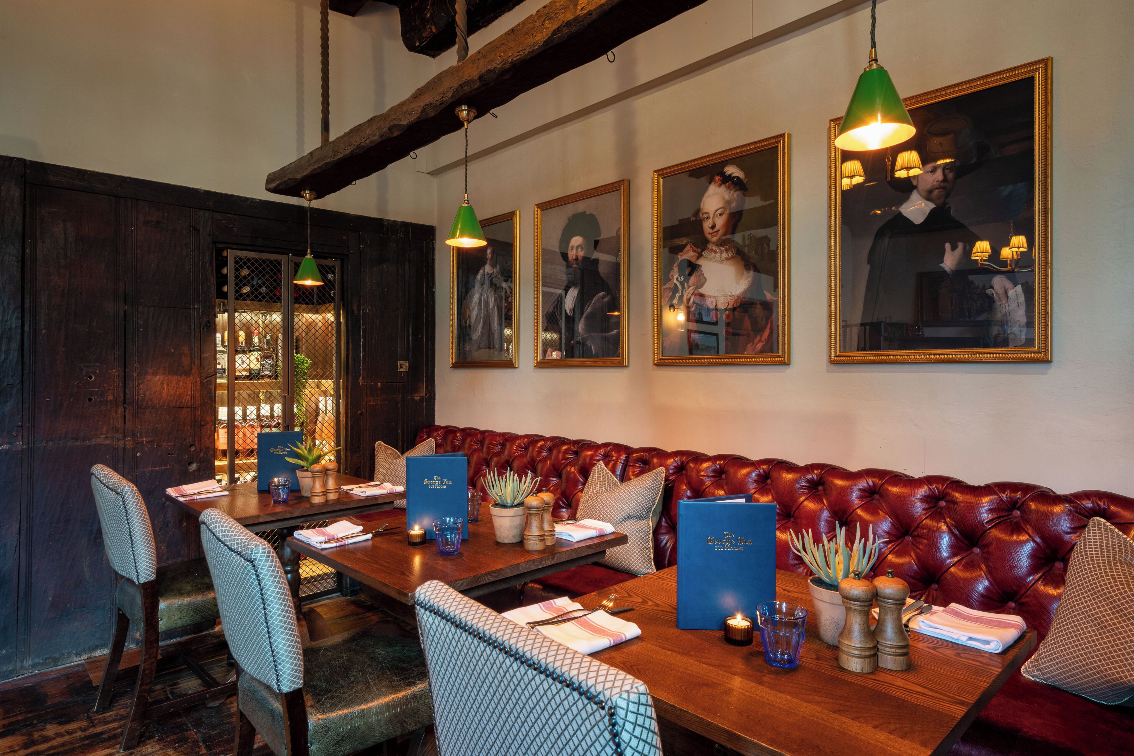 Ein Restaurant mit Holztisch, gedeckten Plätzen, Ledersitzmöbeln und gerahmten Porträts an der Wand.