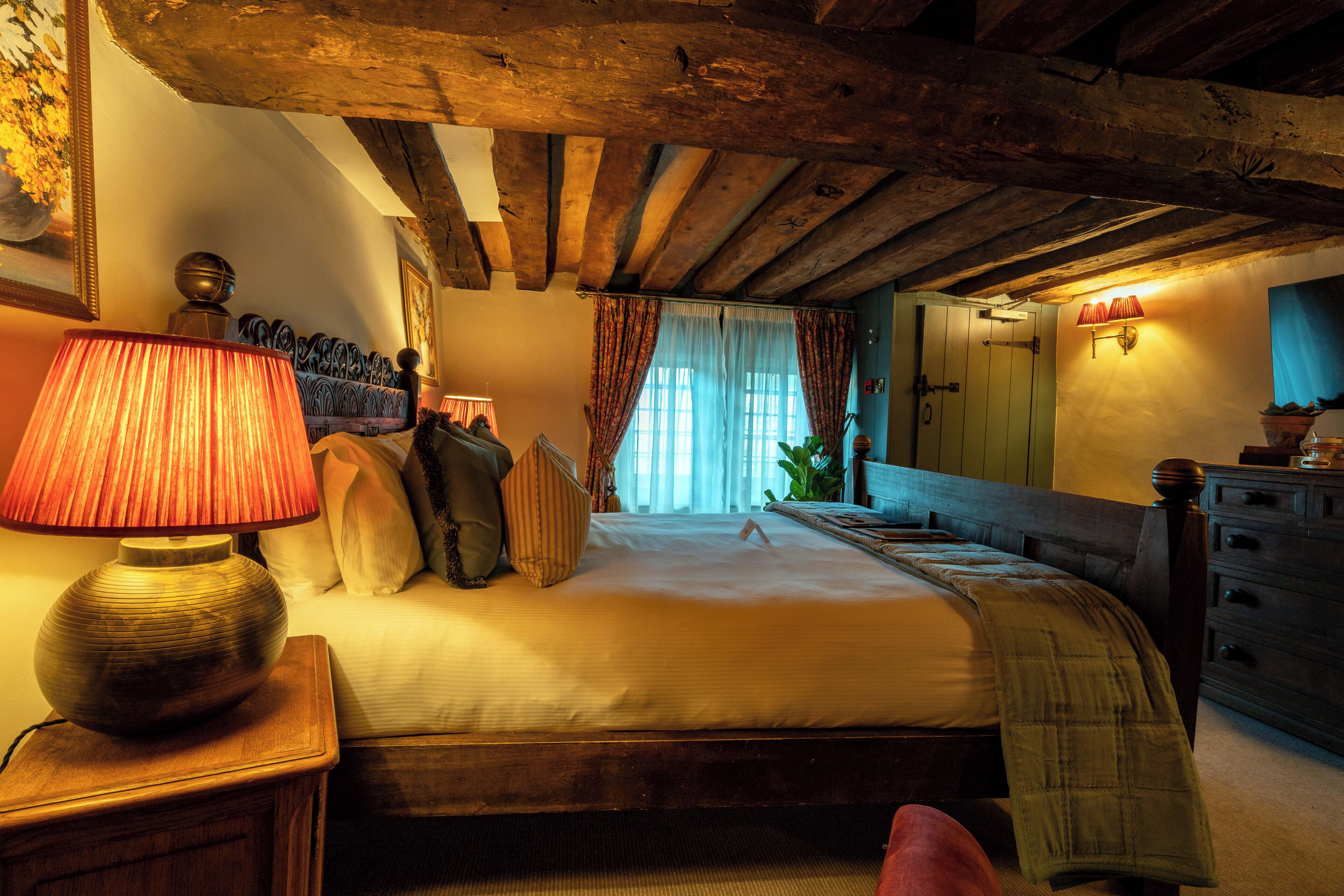 A bedroom with a wooden ceiling, a bed with pillows, a bedside table with a lamp, and a dresser.