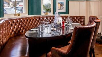 Un comedor con una mesa redonda dispuesta para cuatro personas, rodeado de asientos tipo banca de cuero marrón.