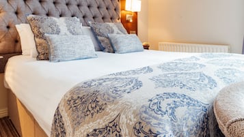 A bedroom with a tufted headboard, a large bed with patterned bedding, a bedside lamp, and a radiator.