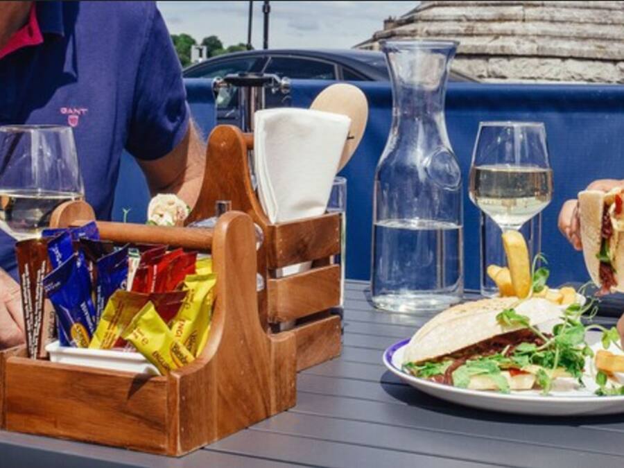 Una mesa con un posavasos de madera, una jarra de vidrio y un plato con un sándwich y papas fritas.