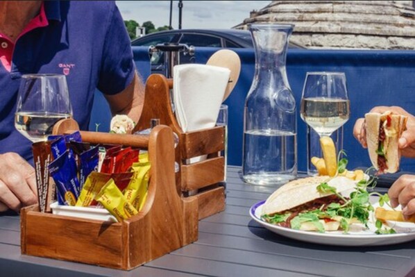 Una mesa con un posavasos de madera, una jarra de vidrio y un plato con un sándwich y papas fritas.