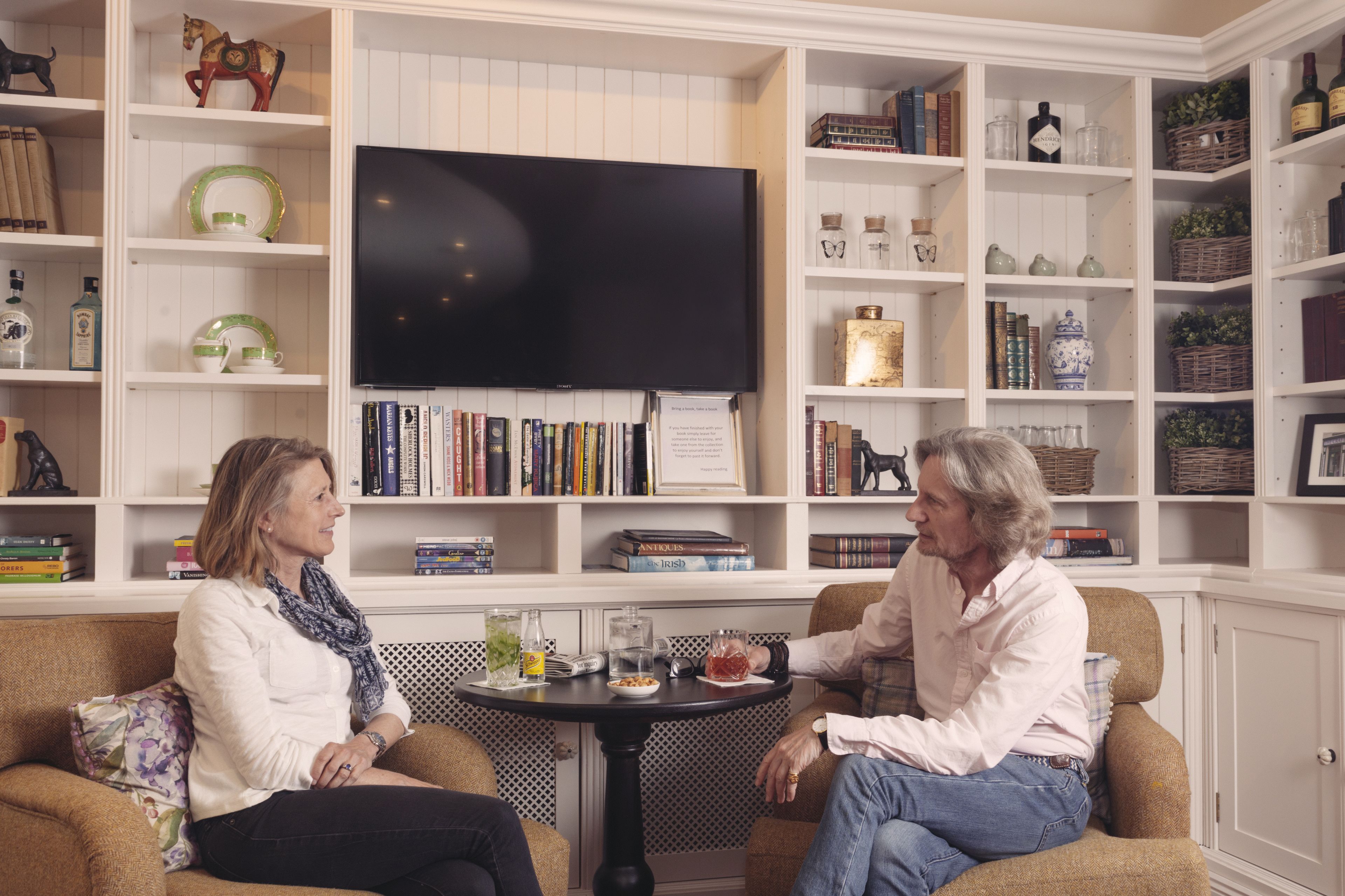 Un salon avec un téléviseur, des étagères à livres et une petite table avec des boissons.
