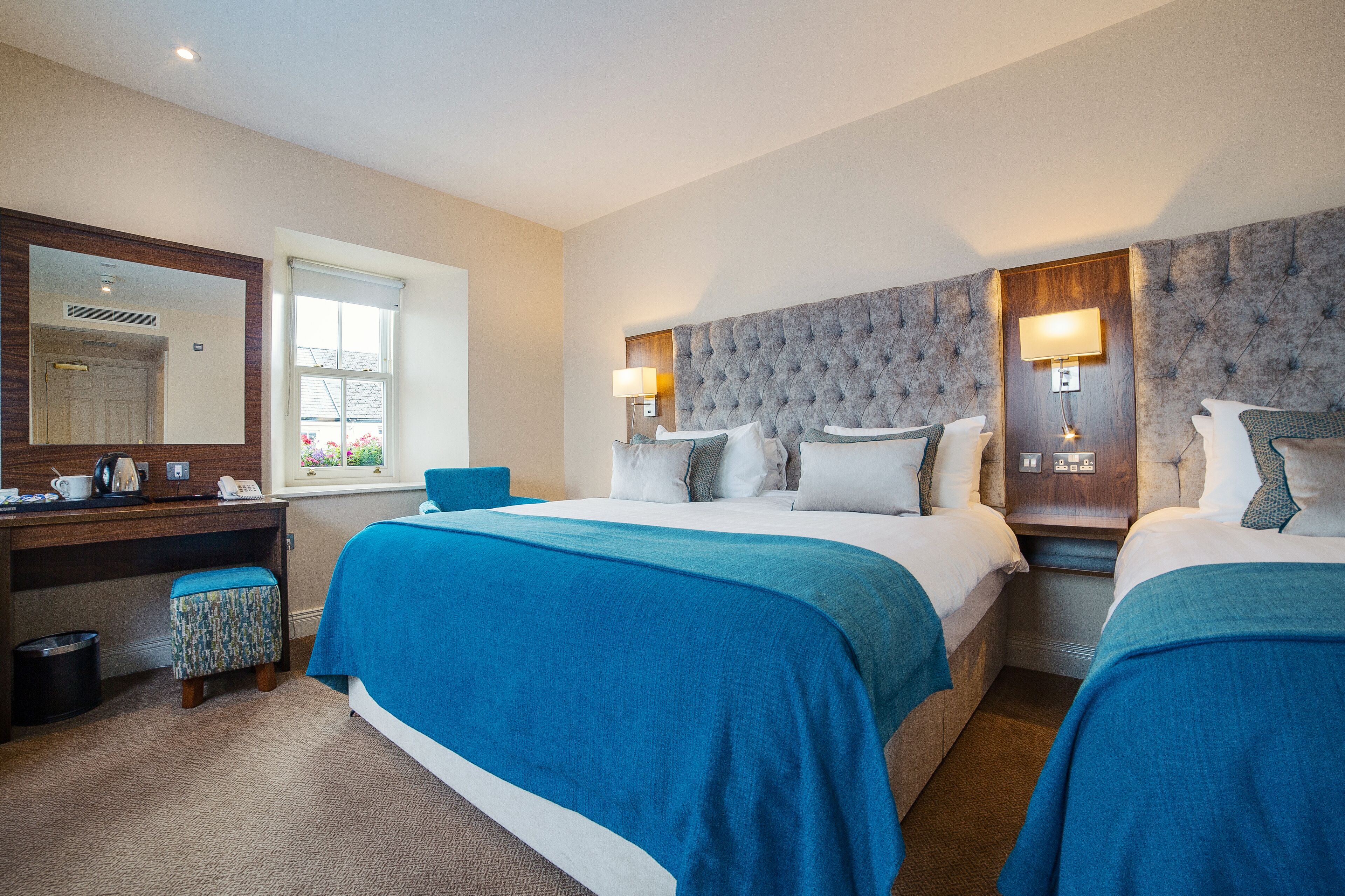 A hotel room with two beds, a desk, a mirror, and a window.