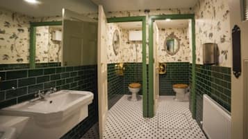 Une salle de bain avec une baignoire, deux toilettes et des miroirs encadrés de vert.